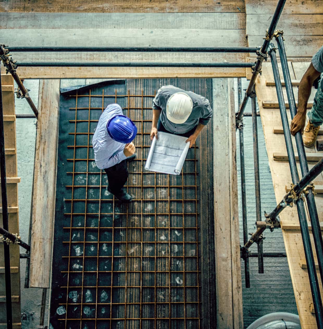 An overhead view of two people in hard hats reviewing plans at a construction site