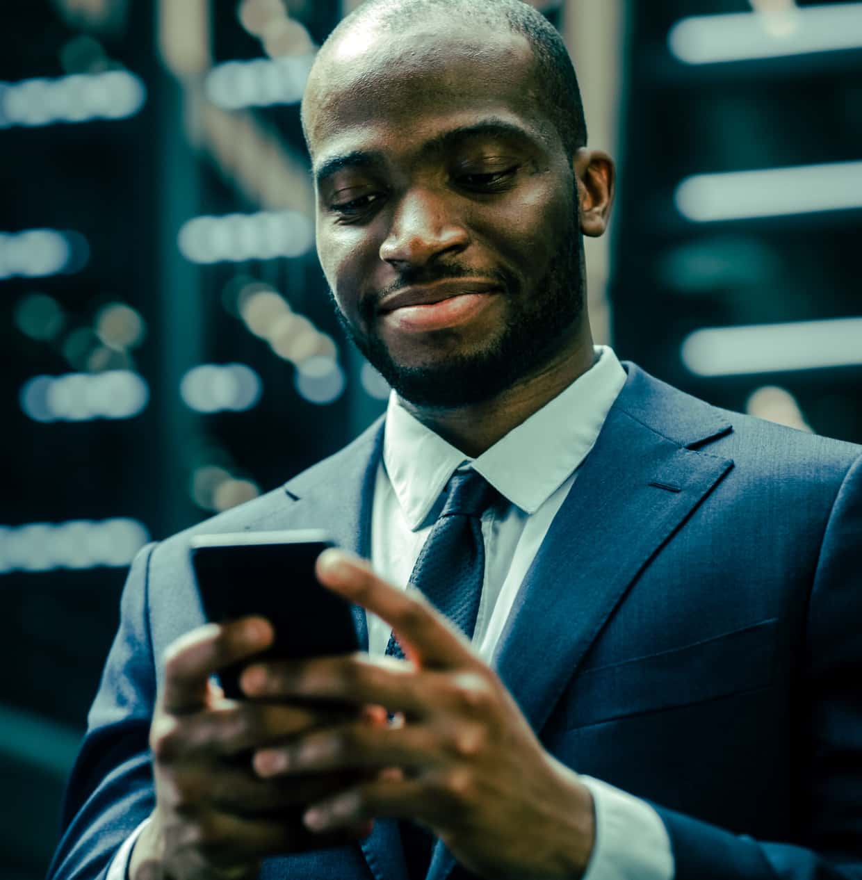 A businessman in a suit smiles while typing on his smartphone.