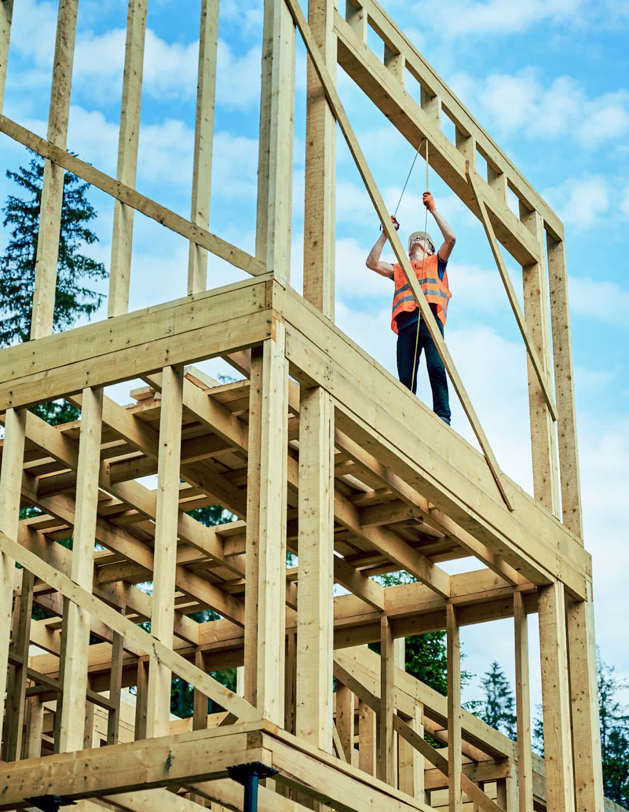 A construction worker stands on the second floor of a partially-framed house.