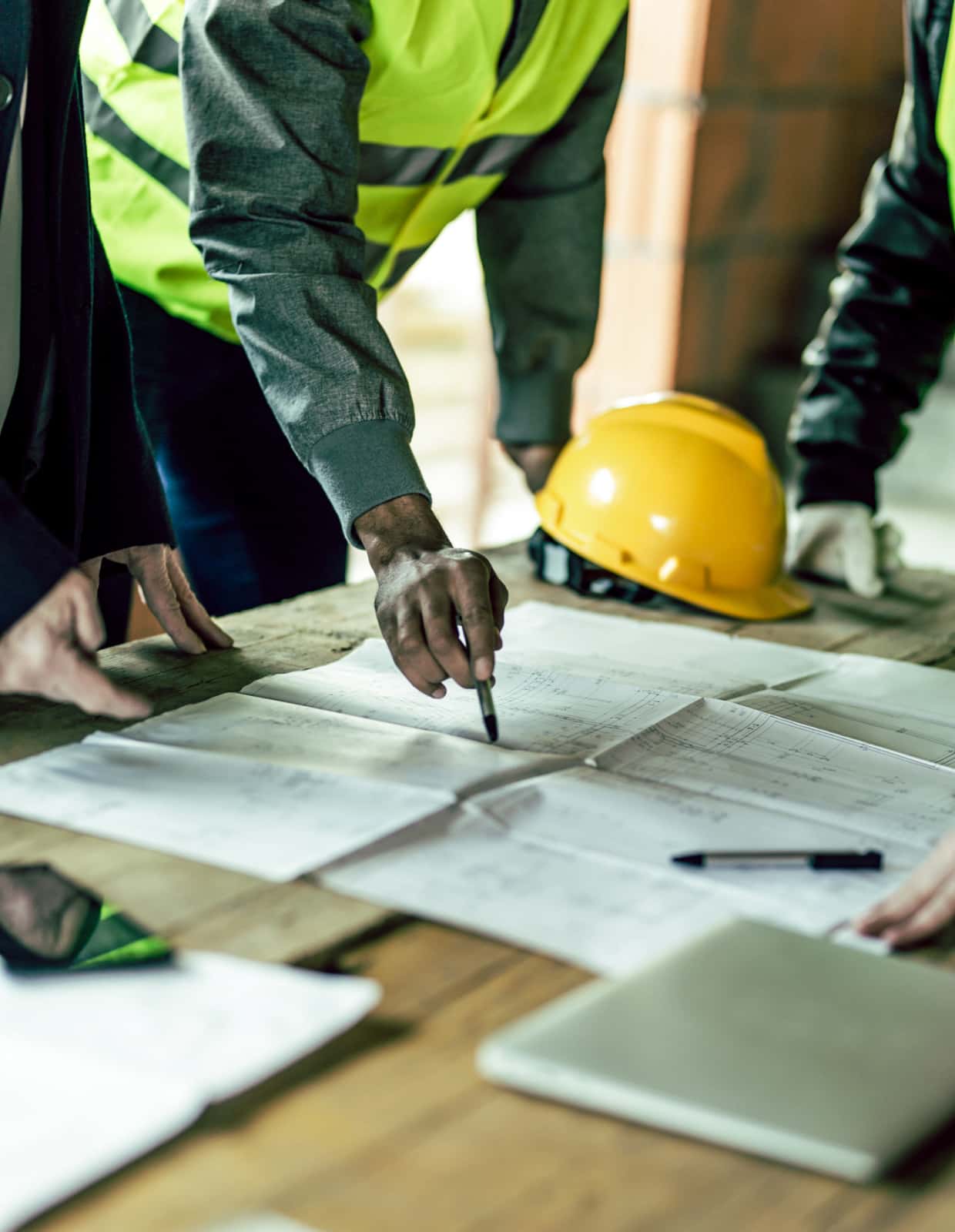 A group of people review plans on a wooden table at a construction site.