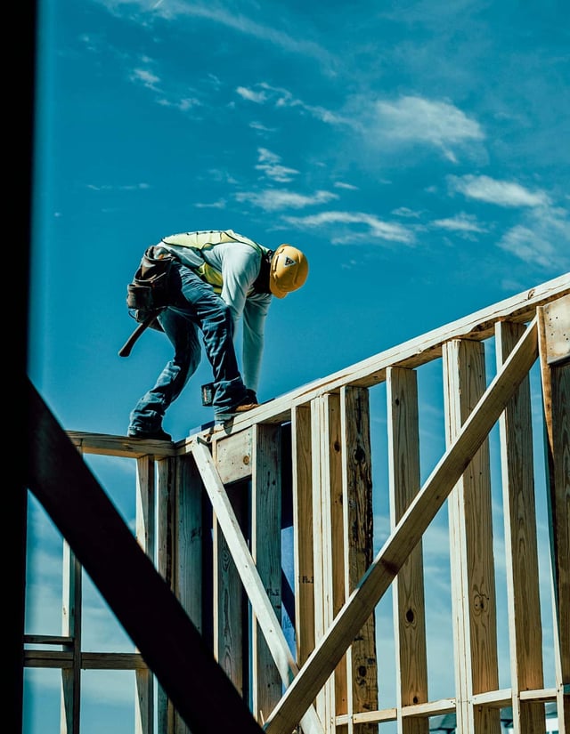 A construction worker stands on top of a wall he is framing.