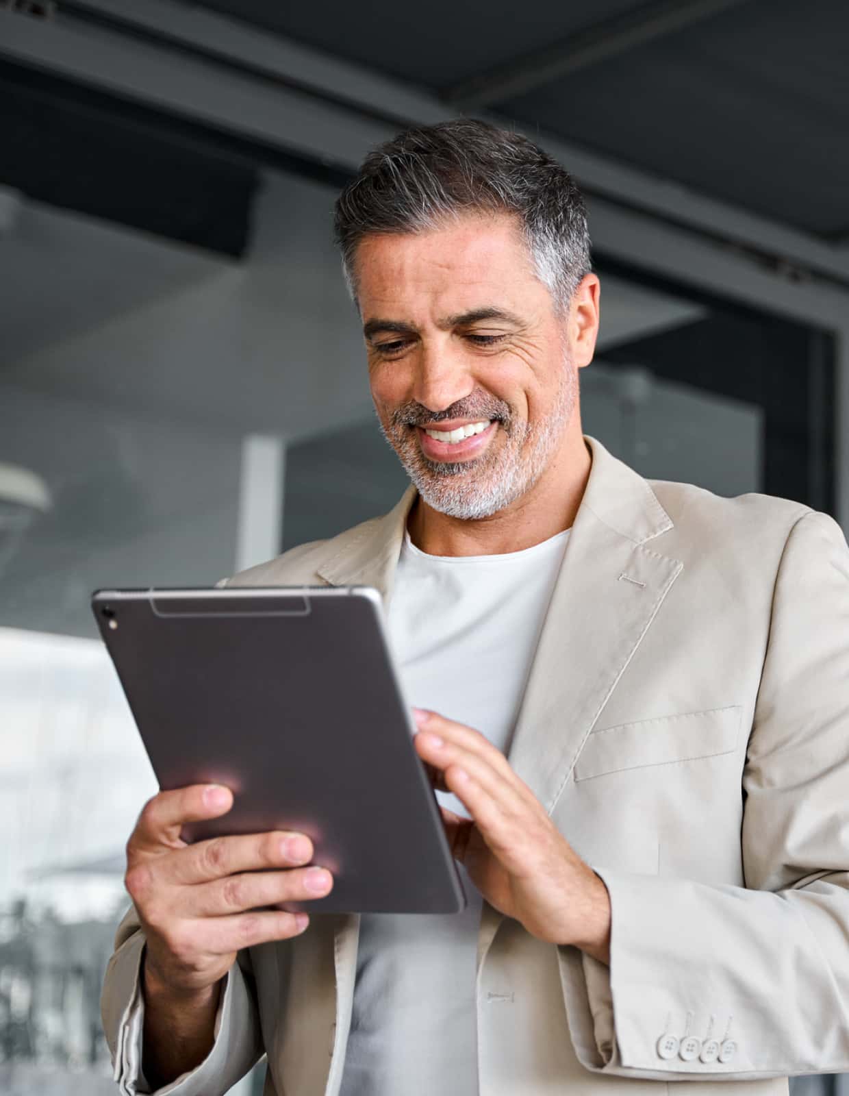 A man in a collared shit and sweater holding a tablet looks off camera.