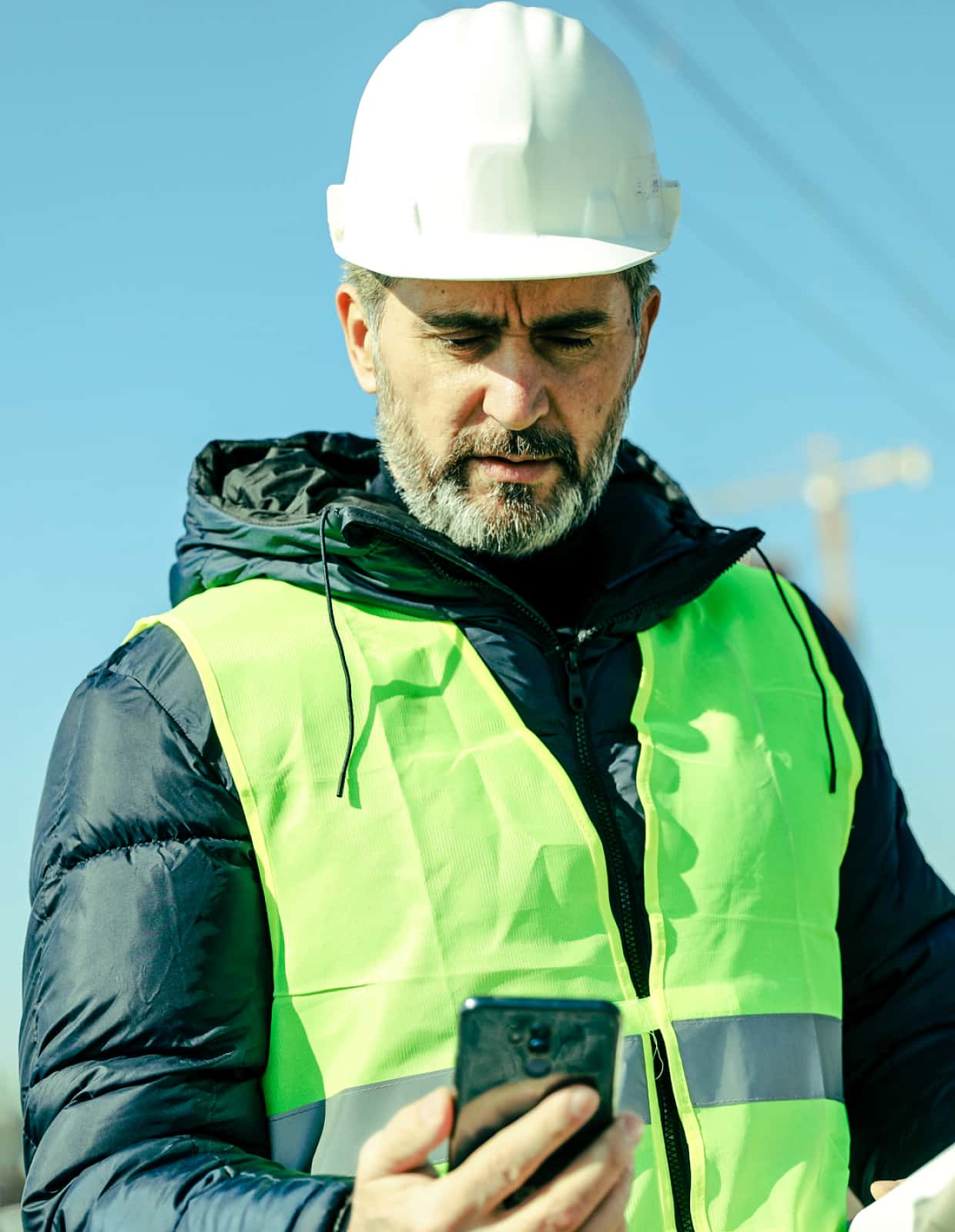 A construction worker in a winter coat looks at a smartphone.