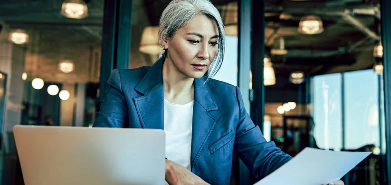Woman reading report next to computer. 