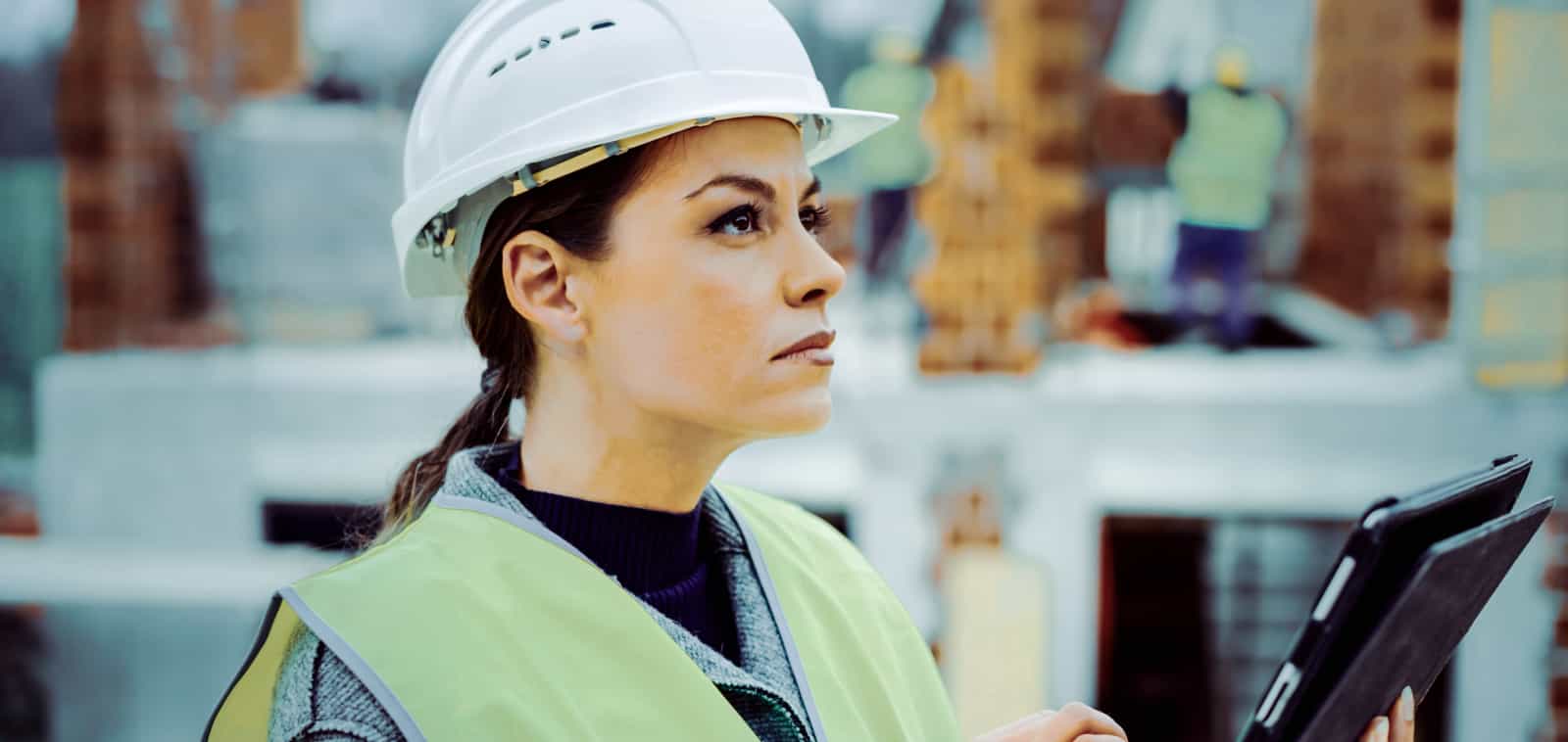 A woman in a hardhat checks a worksite based on information on a tablet.